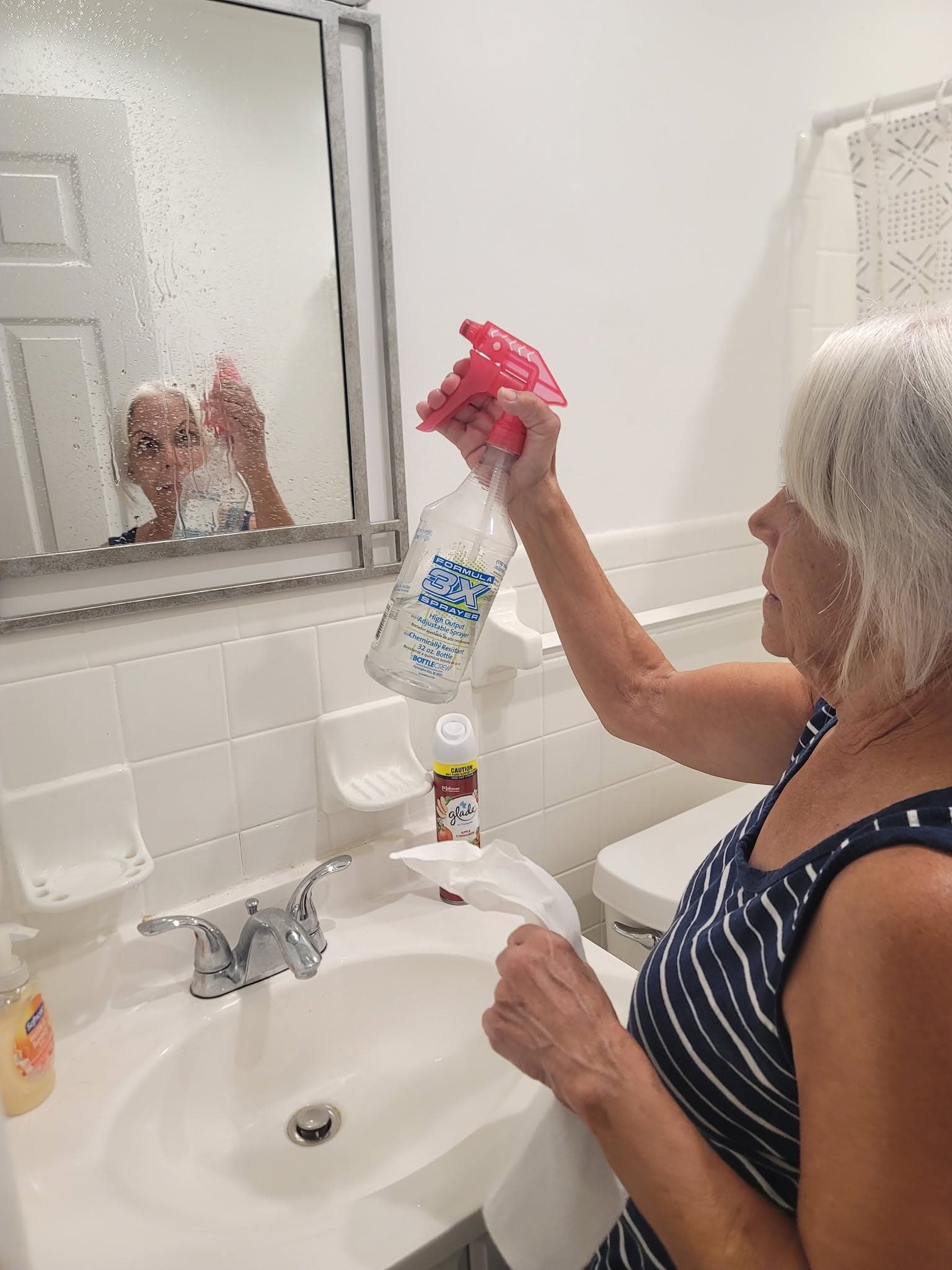 Cleaner spraying and wiping a bathroom mirror