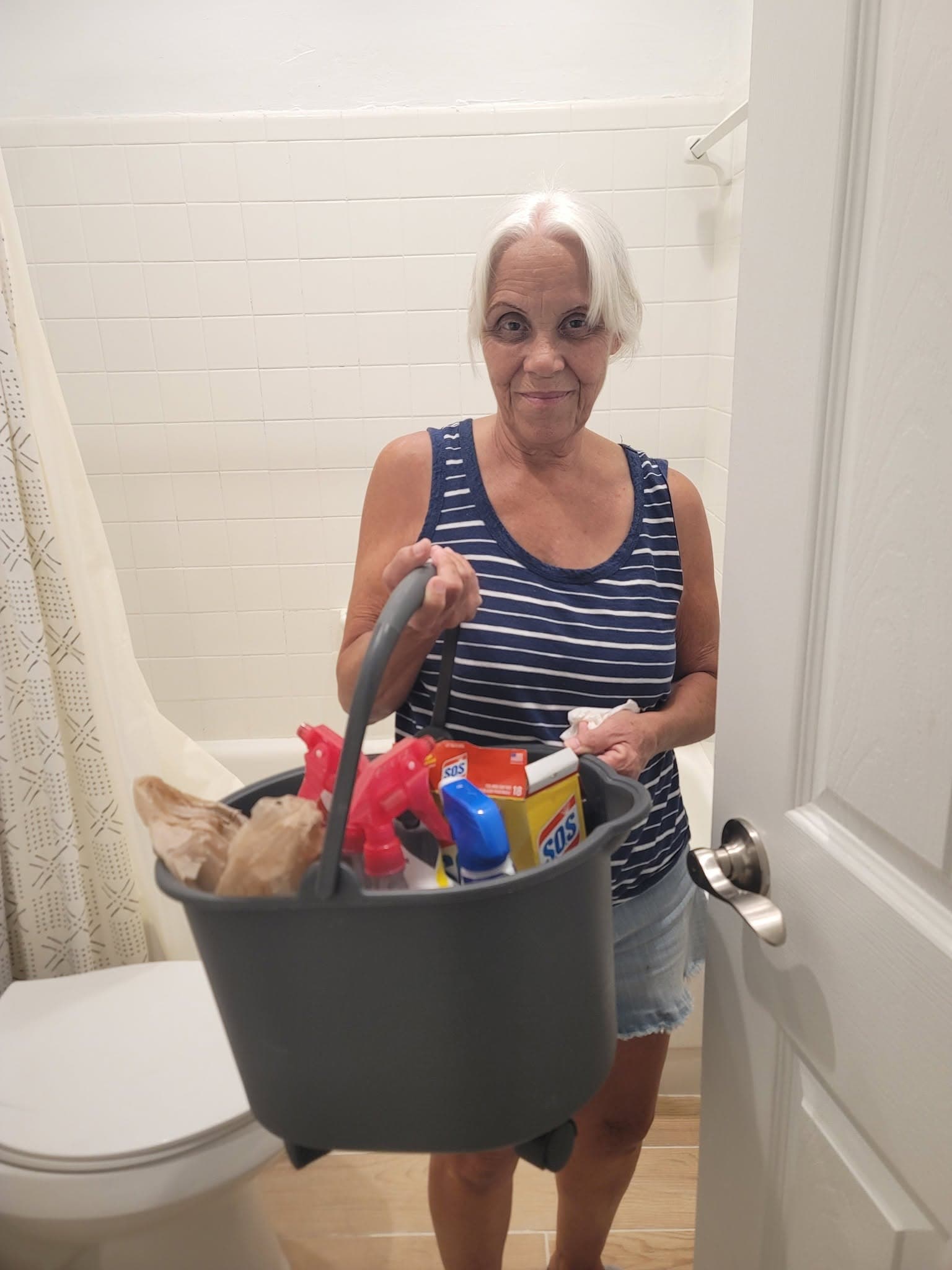 Cleaner holding a bucket of cleaning supplies in a bathroom